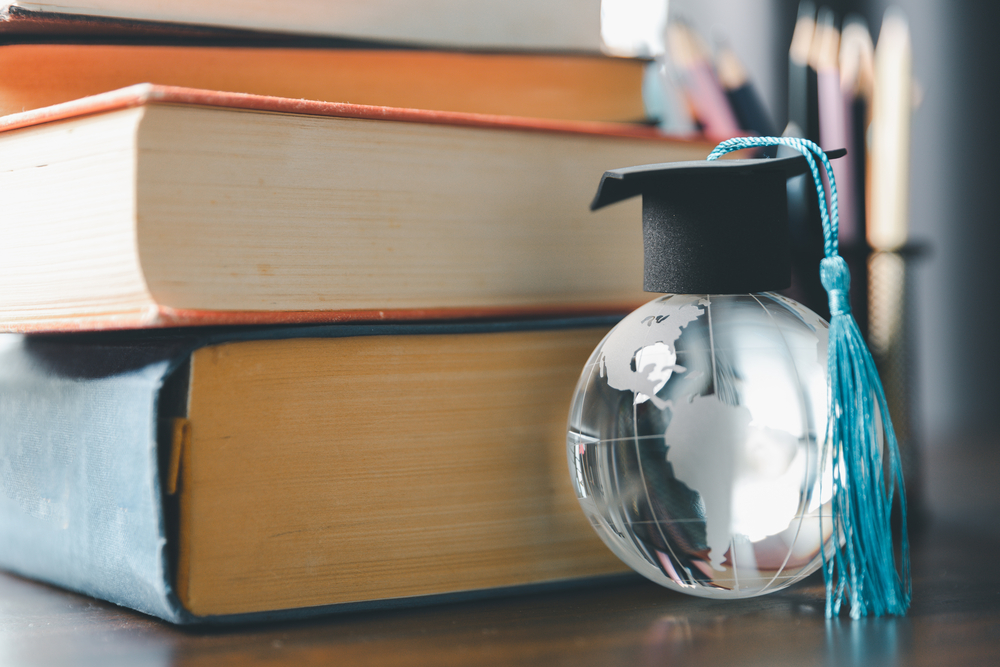 Graduate study abroad program concept : Black graduation cap on a globe map and books, depicts knowledge can be learned online anywhere and everywhere, even in universities or campus around the world.