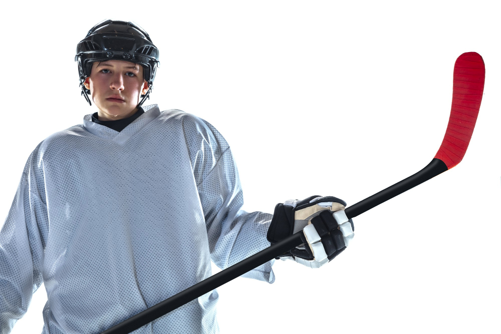 serious young male hockey player with stick ice court white wall
