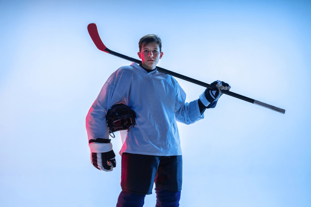 young male hockey player with stick white wall neon light